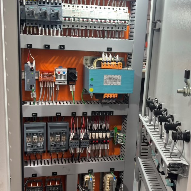 Vista interna de um painel elétrico, com dispositivos, comandos e cabeamento.