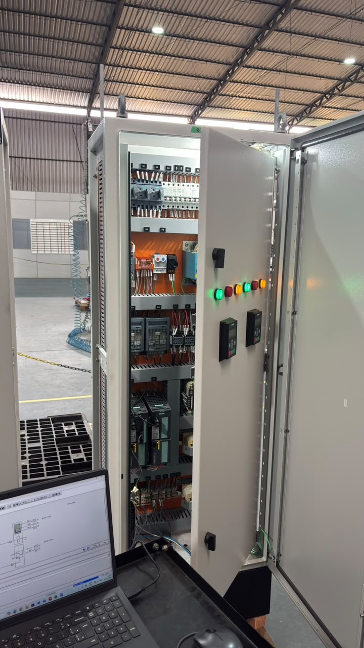 Painel elétrico aberto, com equipamentos e cabeamento internos, e notebook à frente.